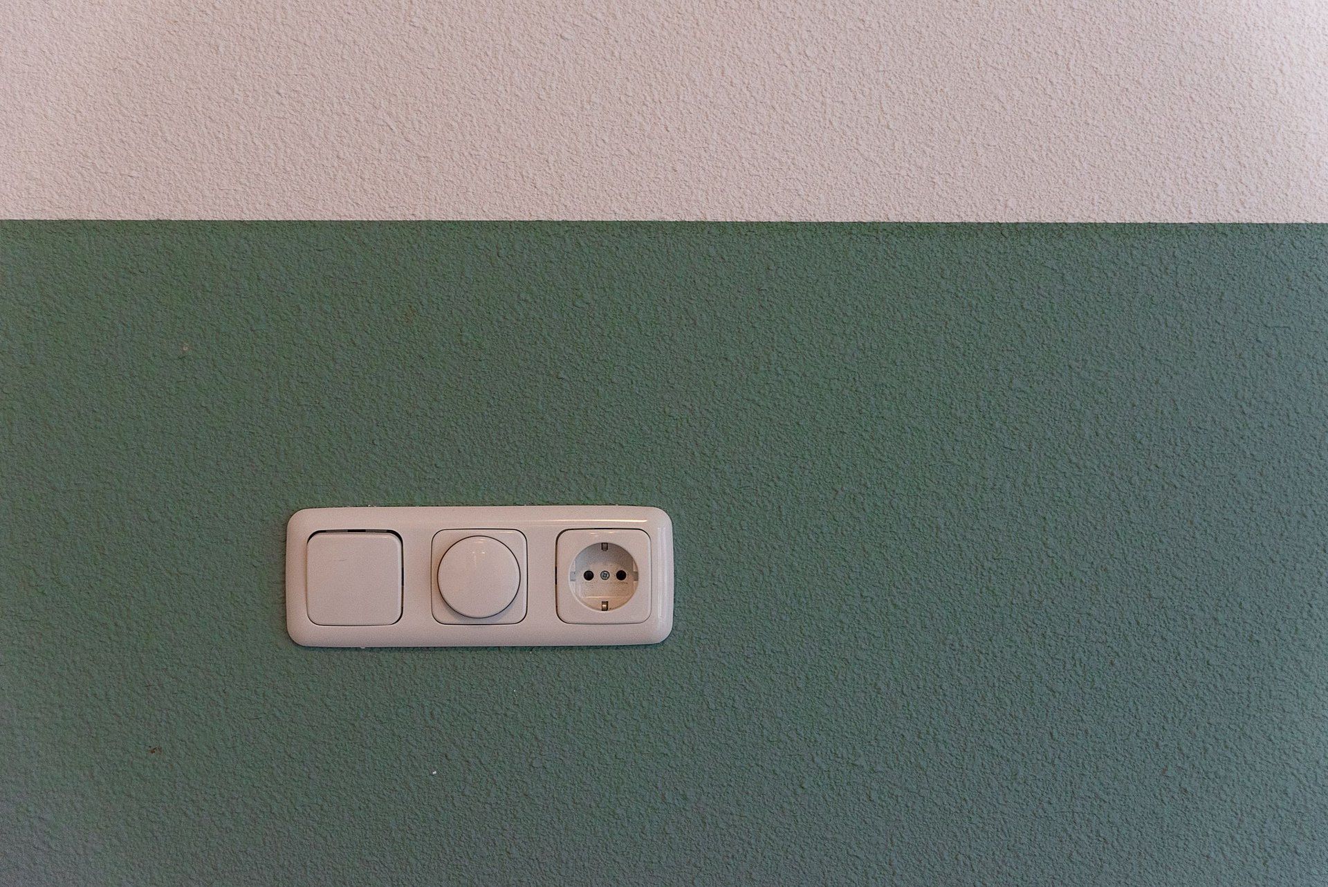 Rahmen mit Lichtschalter, Dimmer und Steckdose an einer grün gestrichenen Wand