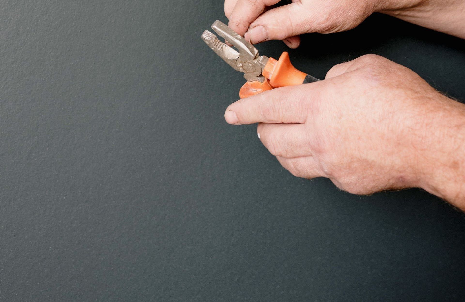 Zwei Hände mit einer Kombizange vor einer anthrazitfarbenen Wand